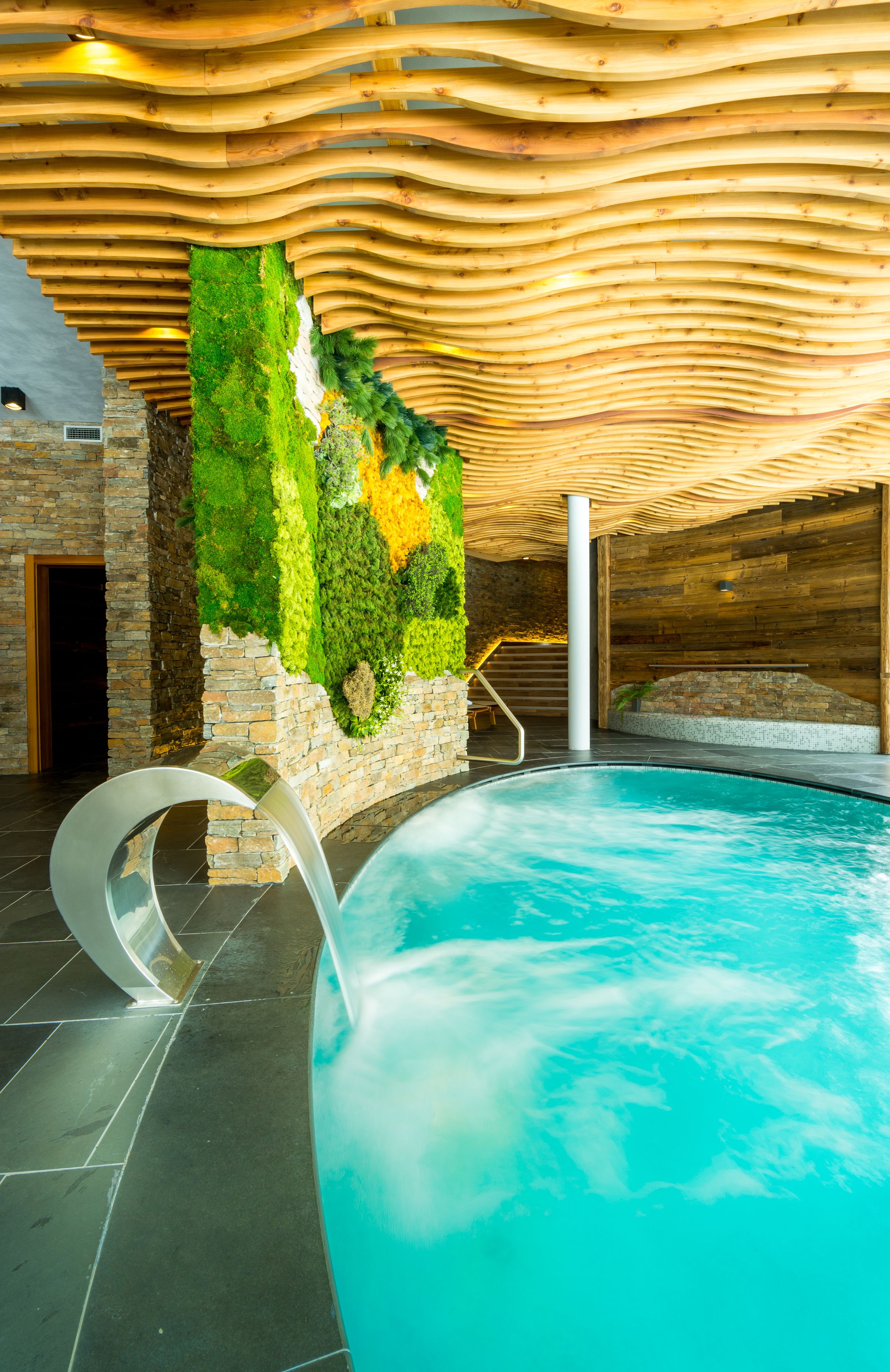 Una piscina interior con techo de madera y pared verde con plantas.