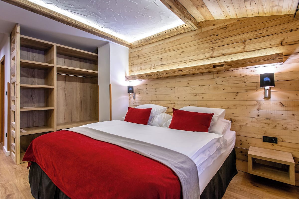 Un dormitorio con paneles de madera, una cama, almohadas rojas y un armario empotrado.