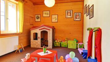 Una habitación de madera con una casita de juegos, muebles rojos y blancos y una ventana con cortinas amarillas.