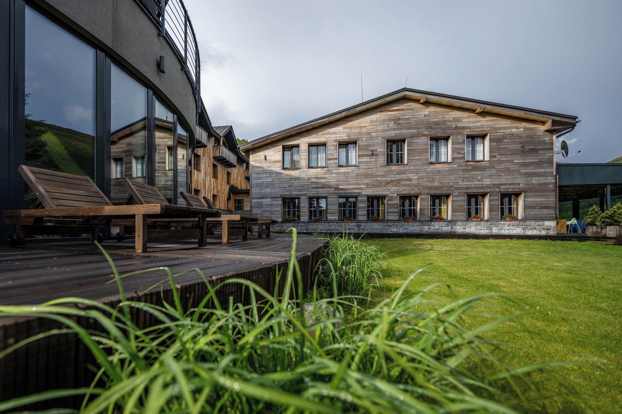 Un edificio moderno con ventanas amplias, una terraza con asientos y un césped bien cuidado.