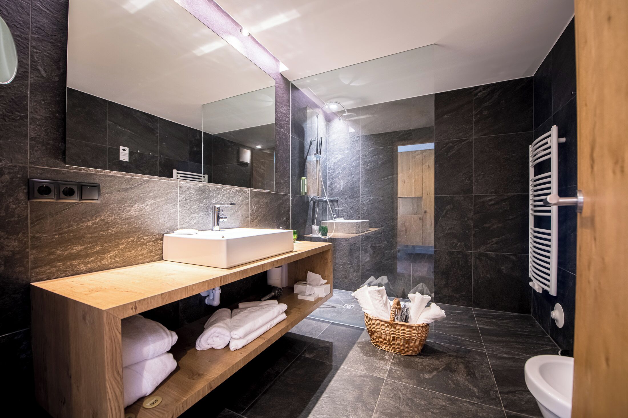 Une salle de bain moderne avec un grand miroir, un meuble-lavabo en bois, un lavabo blanc et un espace douche.