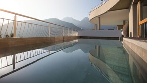 A modern pool with a glass floor, surrounded by a curved building with a railing. - Kronplatz Resort Hotel Kristall (Valdaora)