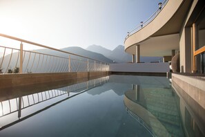 Une piscine moderne dotée d’un plancher en verre, entourée d’un bâtiment aux lignes courbes et agrémentée d’une balustrade.