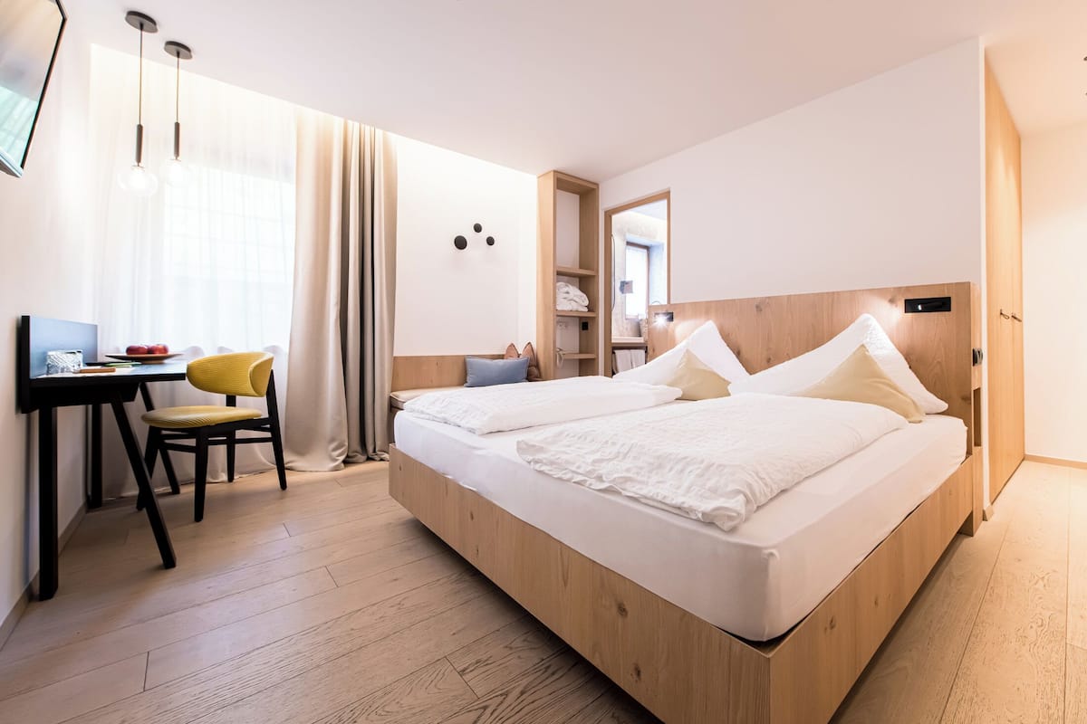 Ein modernes Hotelzimmer mit einem hölzernen Bett, einem Schreibtisch mit Stuhl und einem großen Fenster mit Vorhängen.