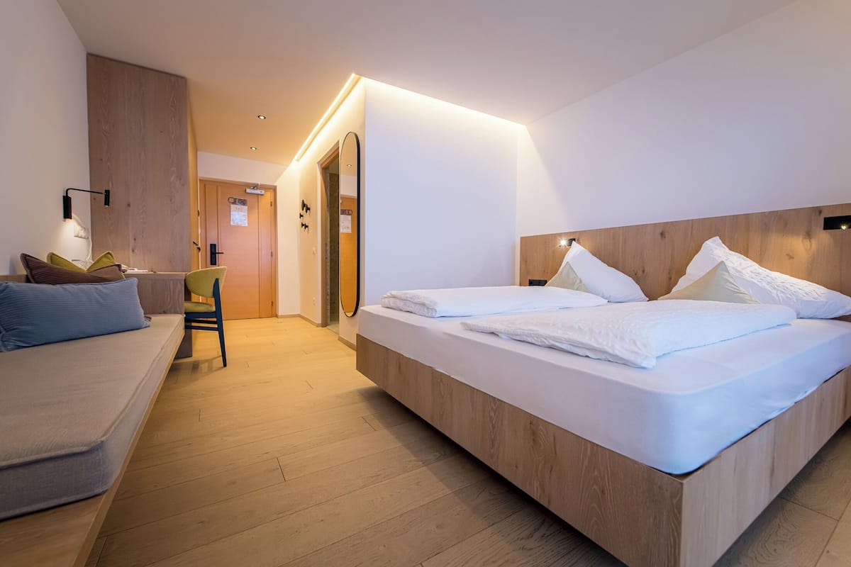 Ein modernes Hotelzimmer mit einem großen Bett, einem Schlafsofa, einem Sessel und einer Wand mit Holzverkleidung.
