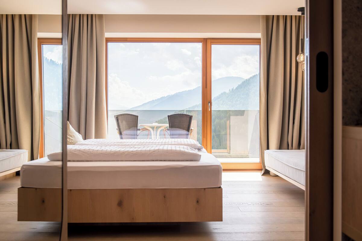 Ein Schlafzimmer mit einem Holzbett, einem Balkon mit Stühlen und Blick auf die Berge.