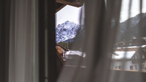 Une vue sur une montagne, visible à travers une fenêtre, avec un bâtiment et une structure en bois qui se détachent au premier plan.