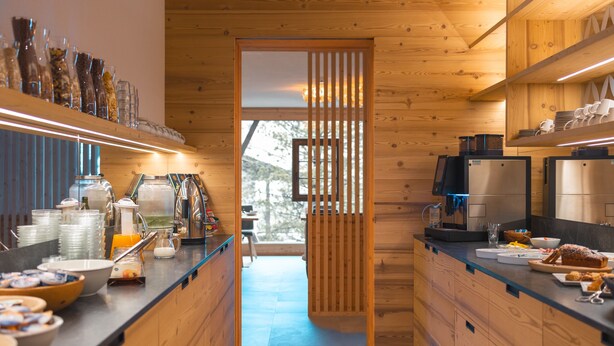Une cuisine moderne avec des meubles en bois, un coin café et une vue sur l’extérieur grâce à une porte coulissante.