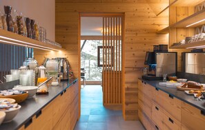 A modern kitchen with wooden cabinets, a coffee station, and a view through a sliding door. - Garni Residence Alnö - Adults Only (Marebbe)