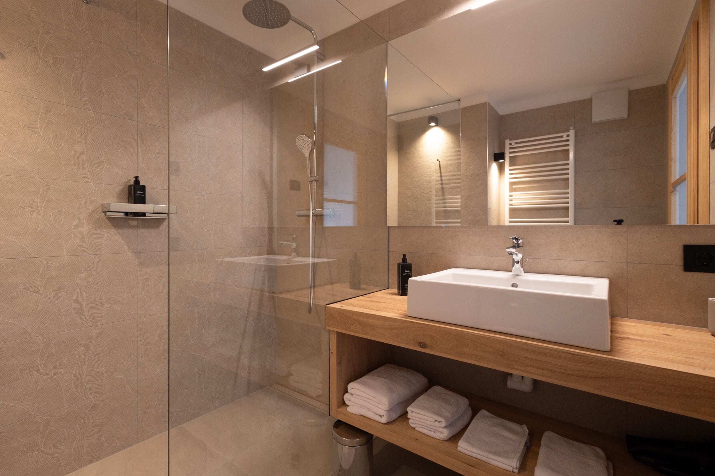 Un bagno moderno con doccia vetrata, mobile bagno in legno con lavello e uno specchio che riflette la zona doccia.