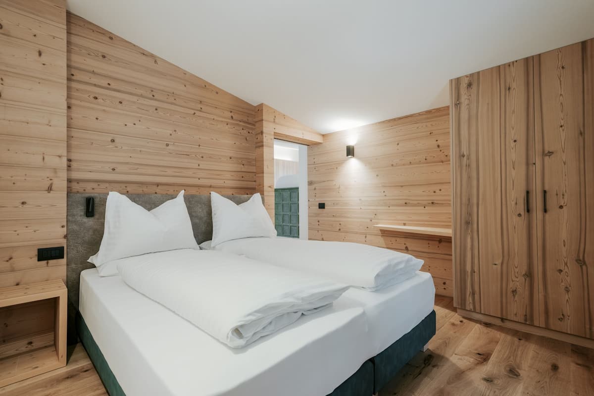 Ein Zimmer mit Holzwandverkleidung, einem Bett mit weißer Bettwäsche, einem Nachttisch und einem Kleiderschrank.
