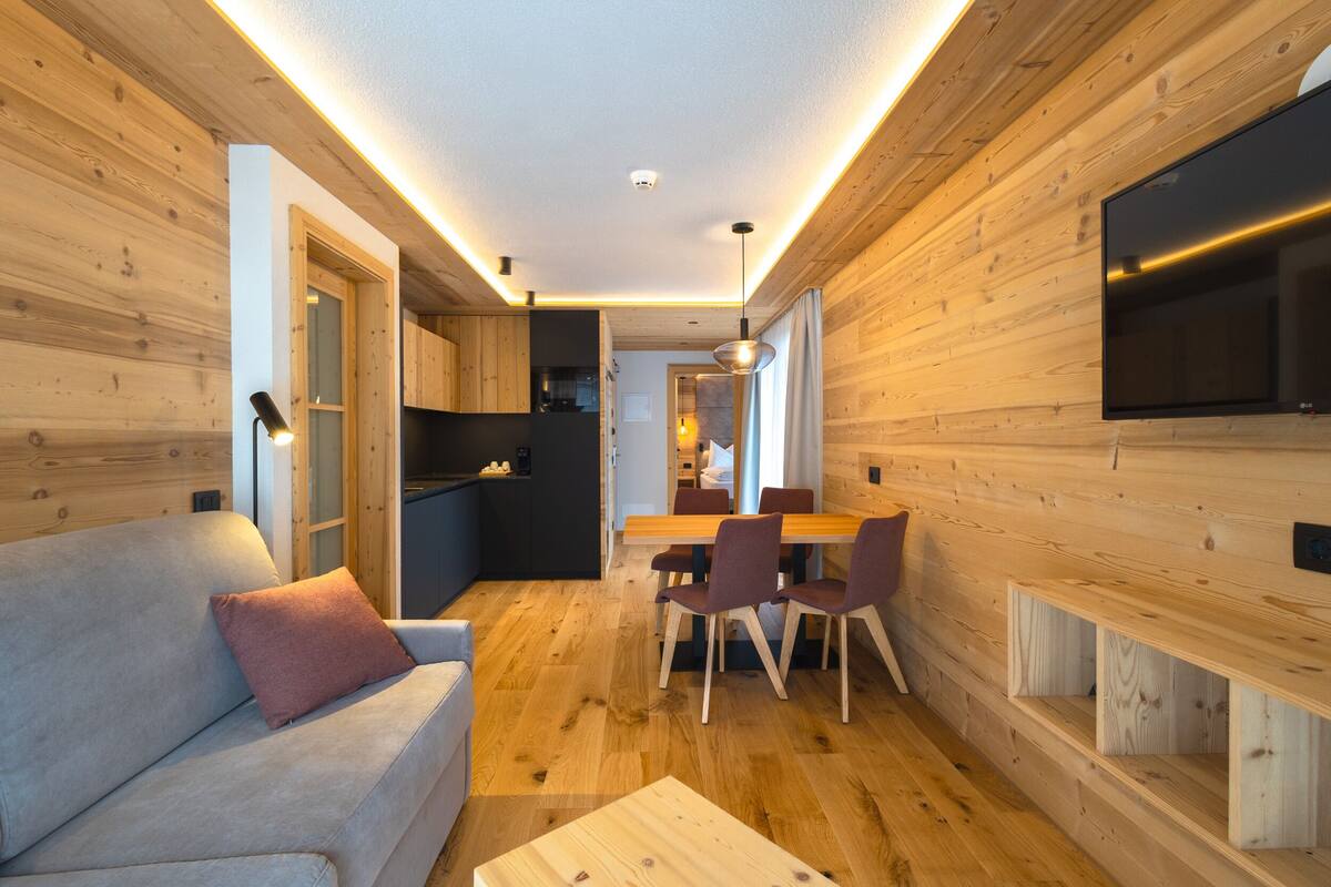 Ein modernes Interieur mit Holzwänden, einer Couch, einem Esstisch mit Stühlen und einem an der Wand montierten Fernseher.