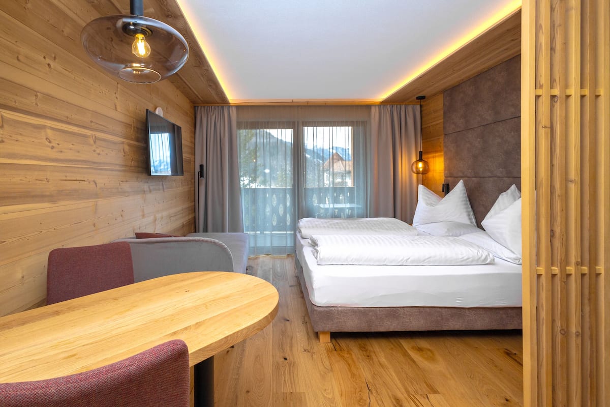 Ein modernes Hotelzimmer mit Holzvertäfelung, einem Bett mit weißen Leinen, einem Holztisch und einem an der Wand befestigten Fernseher.