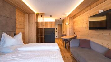 Habitación de hotel moderna con interiores de madera, una cama, un sofá, un comedor y un televisor montado en la pared.