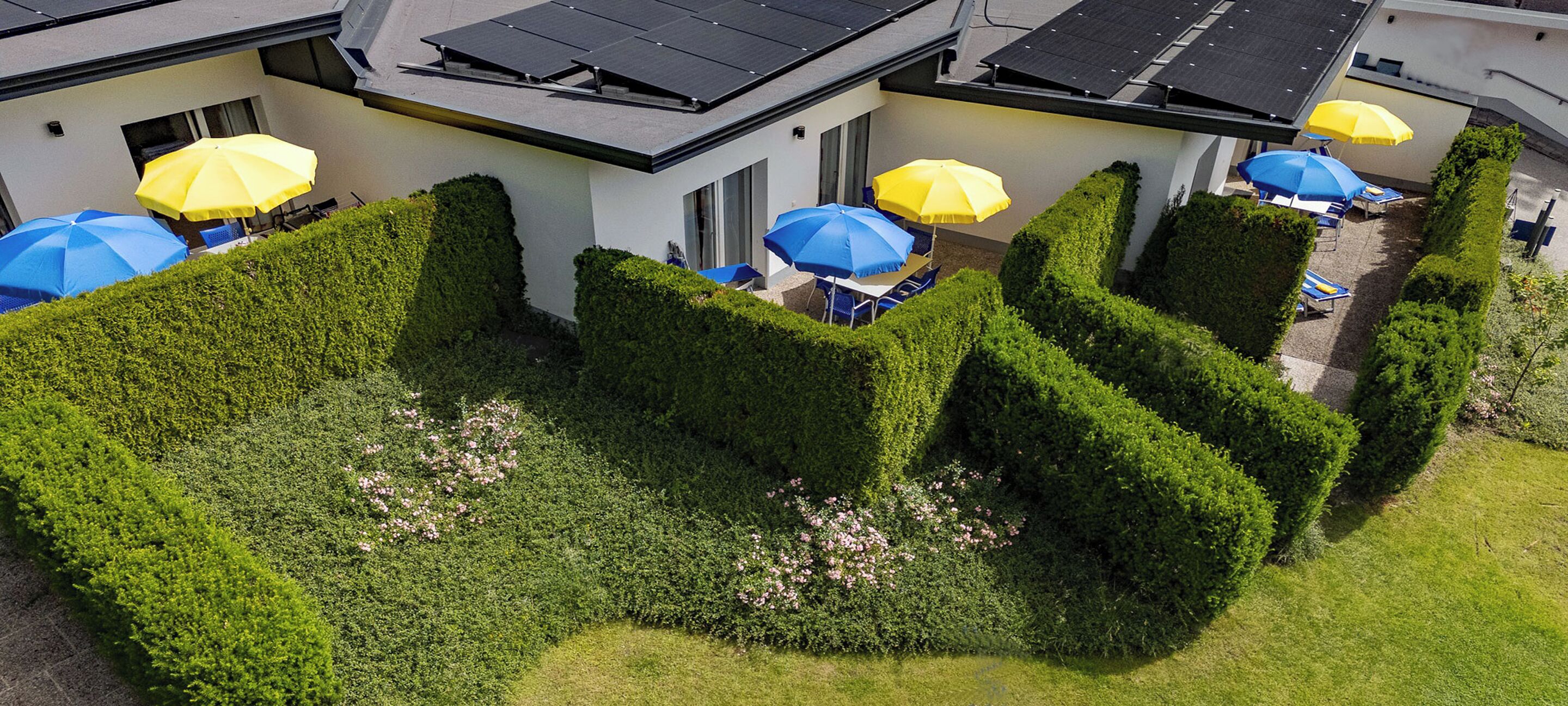 Un jardín bien cuidado con setos ordenados y una zona de estar con sombrillas azules y amarillas.