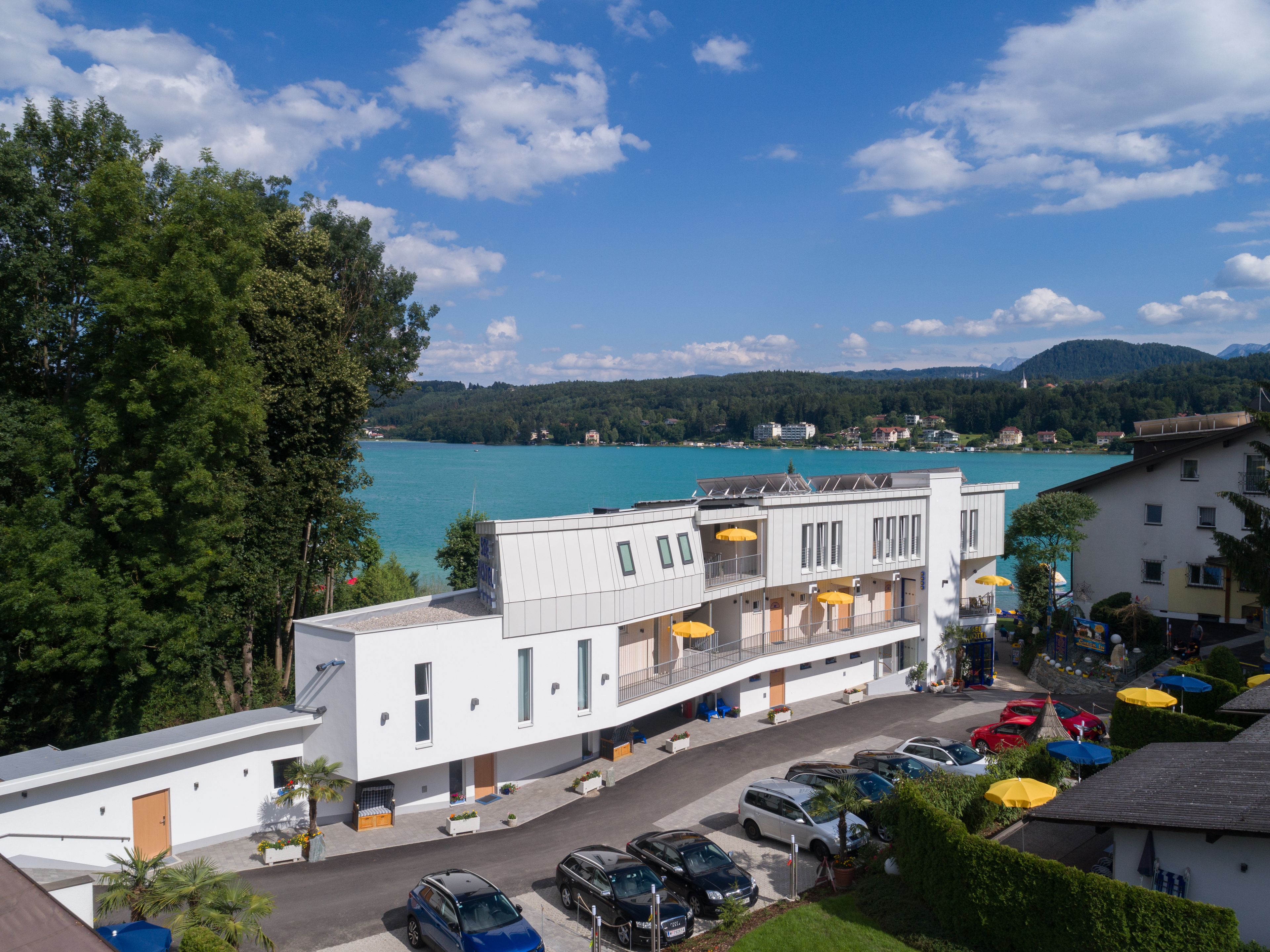 A modern building with a balcony, a parking area, and a view of a lake.