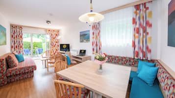Una sala de estar acogedora con una mesa de comedor de madera, sofás coloridos con estampados y un televisor sobre un mueble.