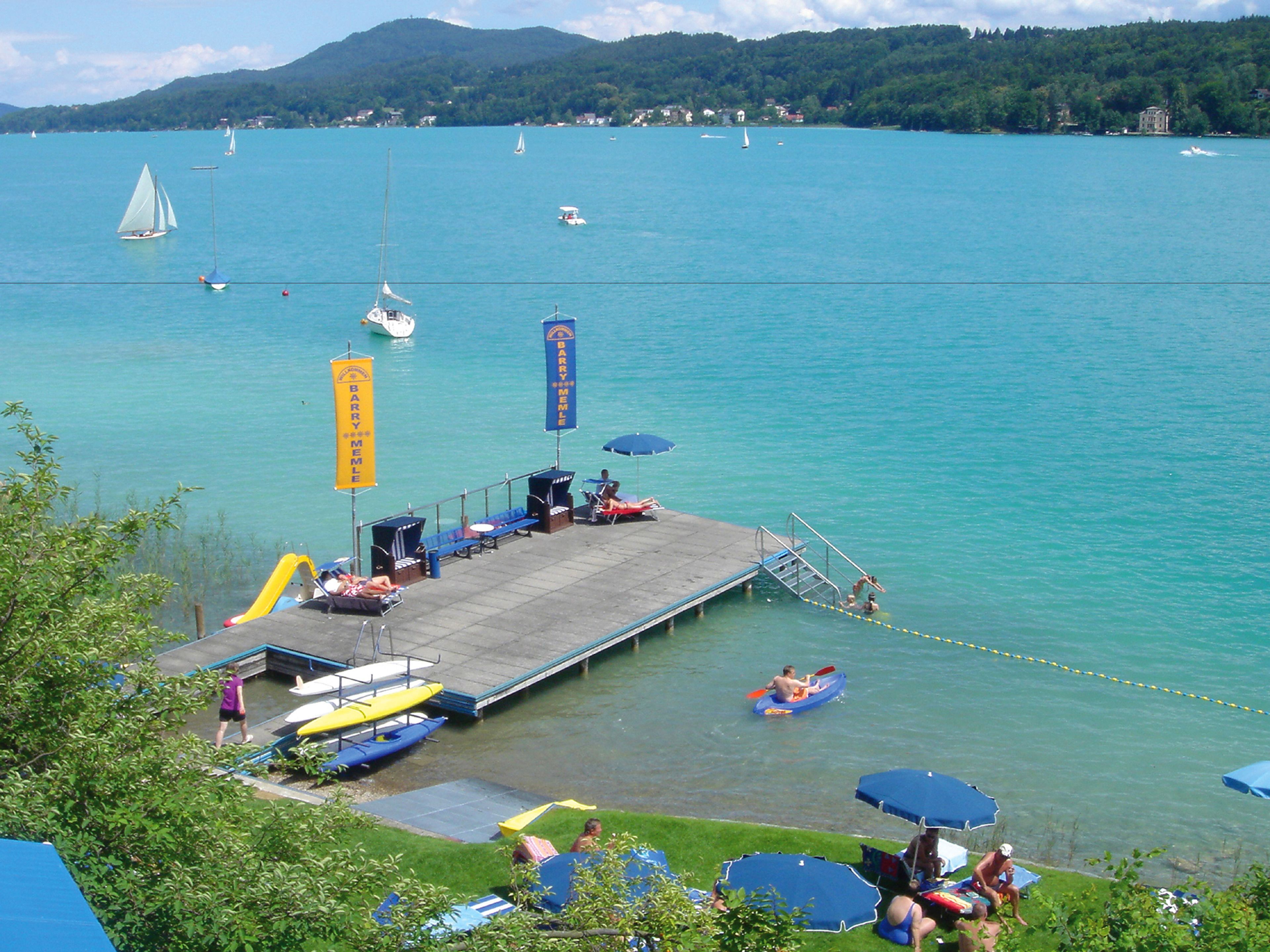 Un muelle sobre el lago con sillas de descanso, sombrillas y una zona para nadar.