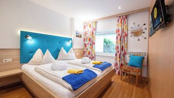 A modern hotel room with a large bed, a wooden headboard, a TV mounted on the wall, and a window with curtains.