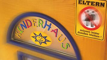 Schild für einen Kinderspielbereich mit Sonne und lächelndem Gesicht, sowie ein Verbotsschild für Erwachsene.