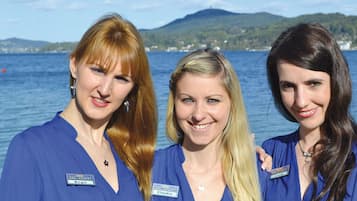Three individuals in blue uniforms with name tags, standing by a body of water with a mountainous backdrop.