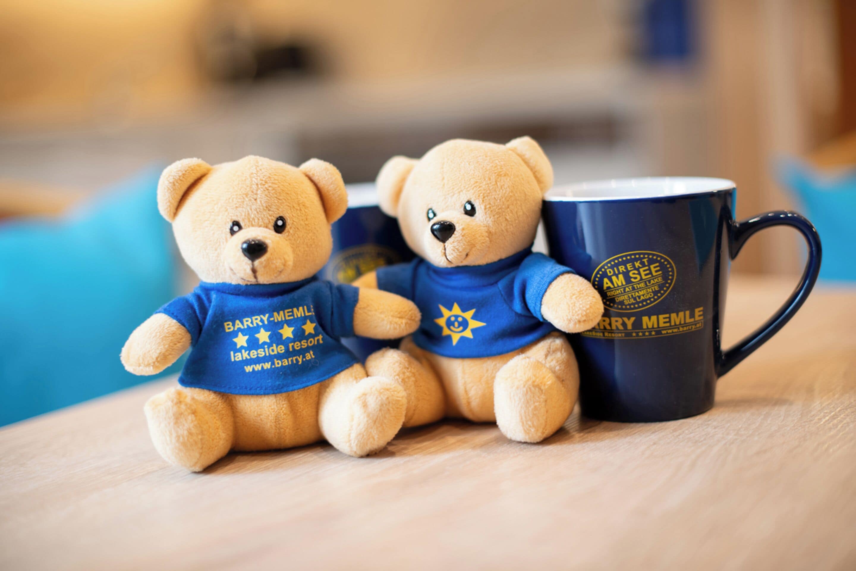 Dos osos de peluche suaves, vestidos con camisas azules con texto, sentados junto a una taza azul oscuro con texto.