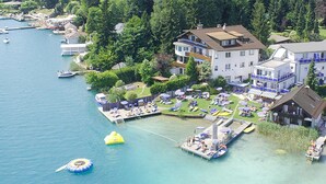 Vue aérienne d’une propriété au bord du lac, avec un quai, des bateaux et un jardin bien entretenu.