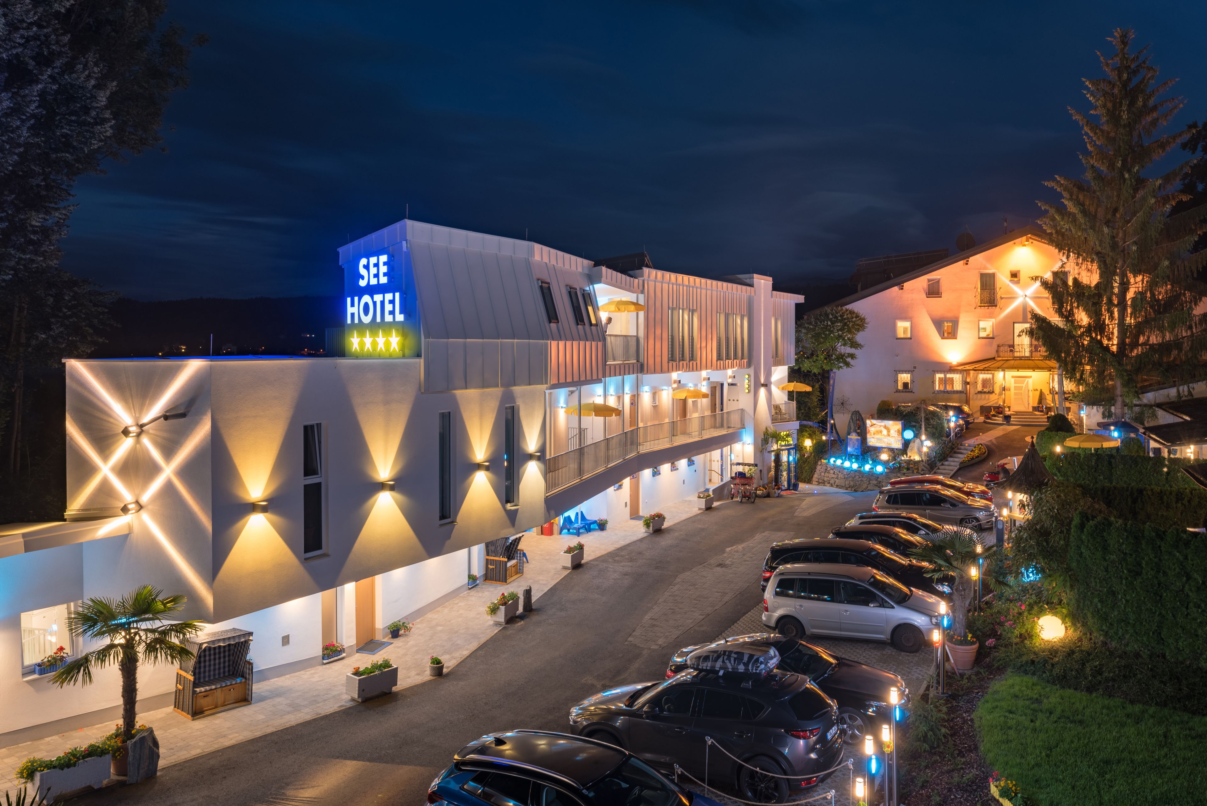 A hotel with a modern design, a visible signboard, and a parking area with multiple cars.