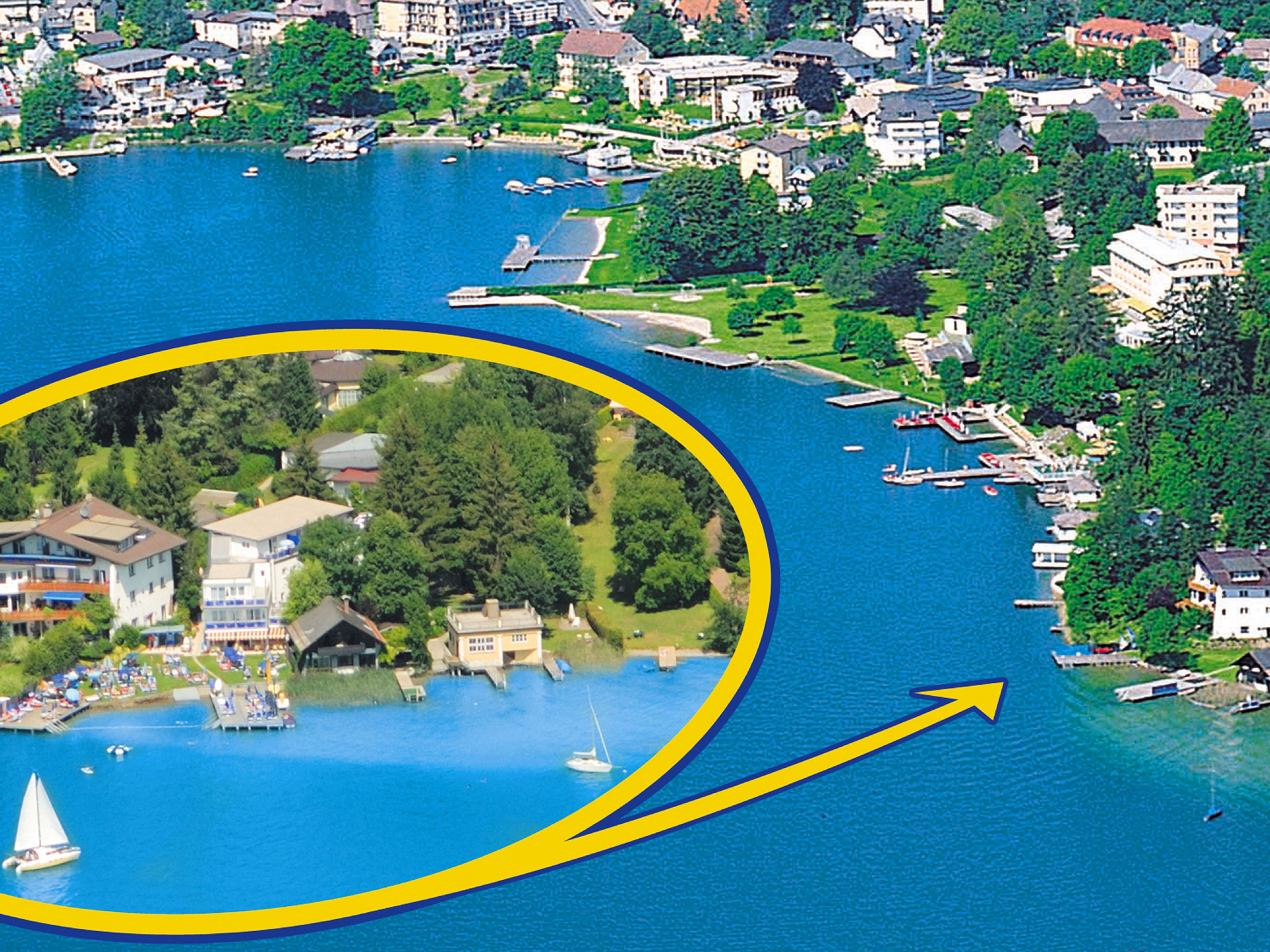 An aerial view of a lakeside town with a highlighted area featuring a residential complex with multiple buildings, a dock, and a sailboat.