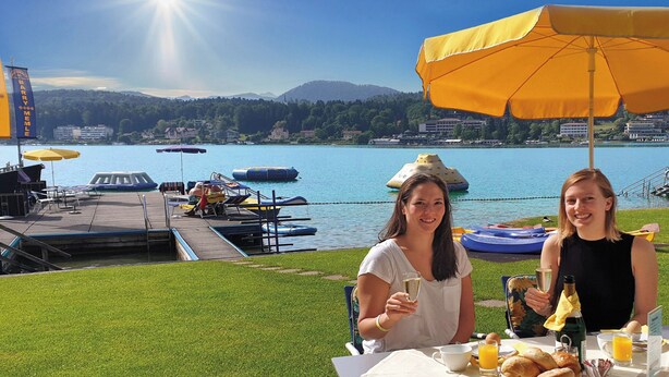 Deux personnes sont assises à une table, devant un lac et des bateaux.