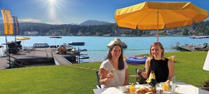 Duas pessoas jantando à mesa com vista para um lago e barcos.