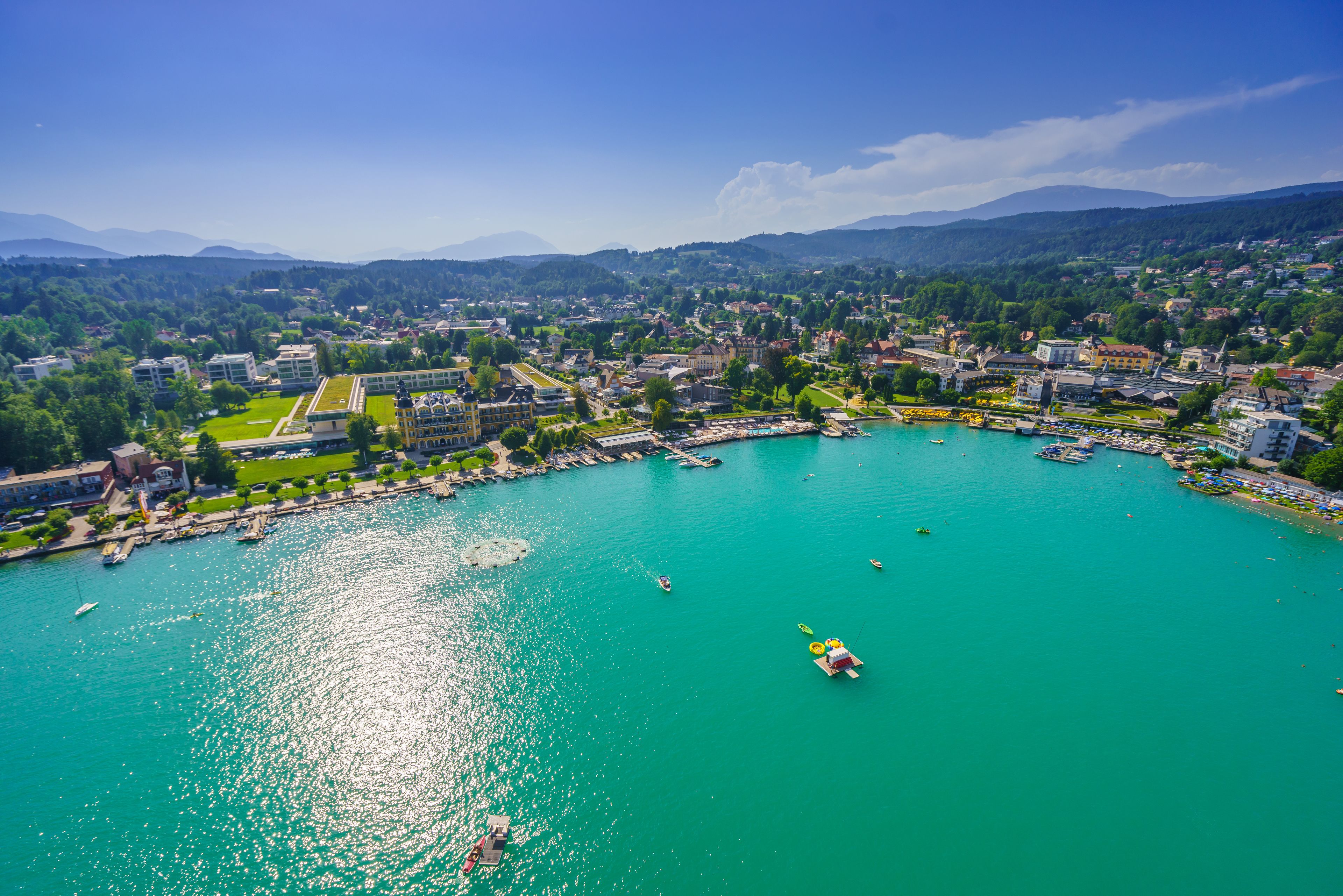 Luftaufnahme einer Küstenstadt mit einer Marina, Gebäuden und einem Bergpanorama im Hintergrund.