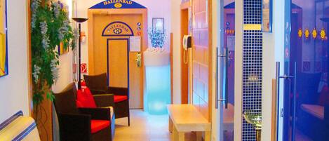 Una hall d'albergo con reception, zona salotto e un angolo doccia in vetro.