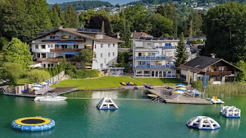 Ein Hotel am Seeufer mit mehreren Gebäuden, einem Steg mit Booten und einem Schwimmbereich mit Luftmatratzen.