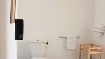 Un baño limpio y minimalista con inodoro blanco, estante de madera, toallero y un cuadro en la pared.