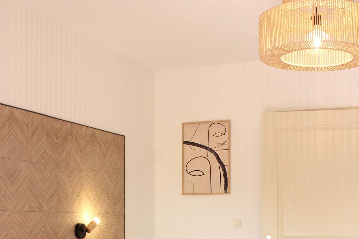 Een net opgemaakt bed met een beige deken, een houten hoofdbord en een wandlamp.