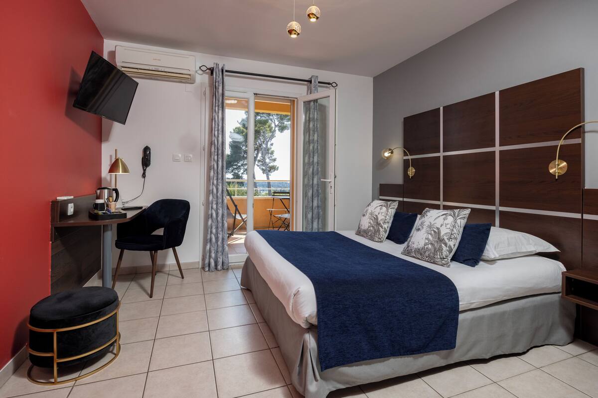 Een slaapkamer met een bed, bureau, stoel, televisie en een balkon met uitzicht.