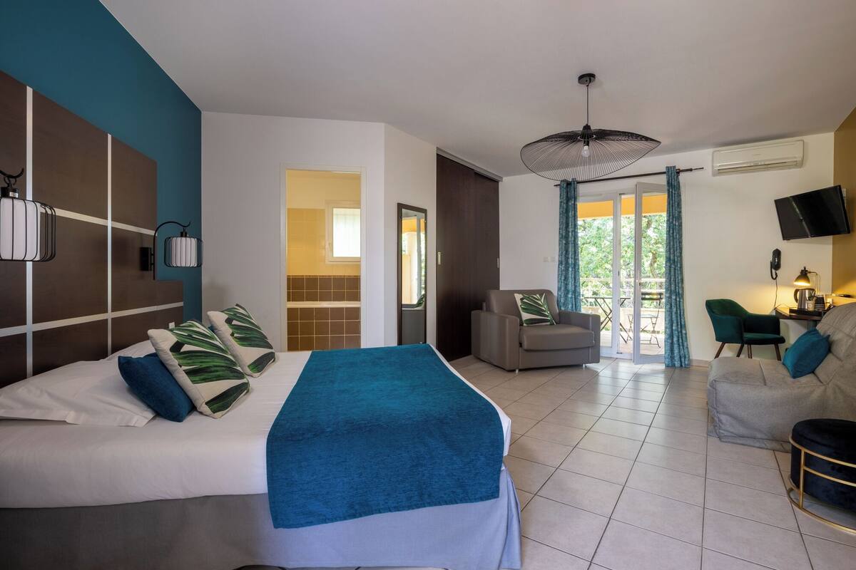 Een moderne hotelkamer met een groot bed, een zithoek met een bank en fauteuils, een televisie en een balkon met uitzicht.