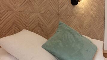 A bed with white bedding and two pillows, one green and one white, against a wooden headboard with a chevron pattern.
