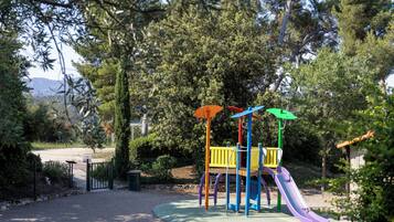 Une aire de jeux avec un toboggan et des structures d’escalade, entourée d’arbres et bordée d’un chemin de gravier.
