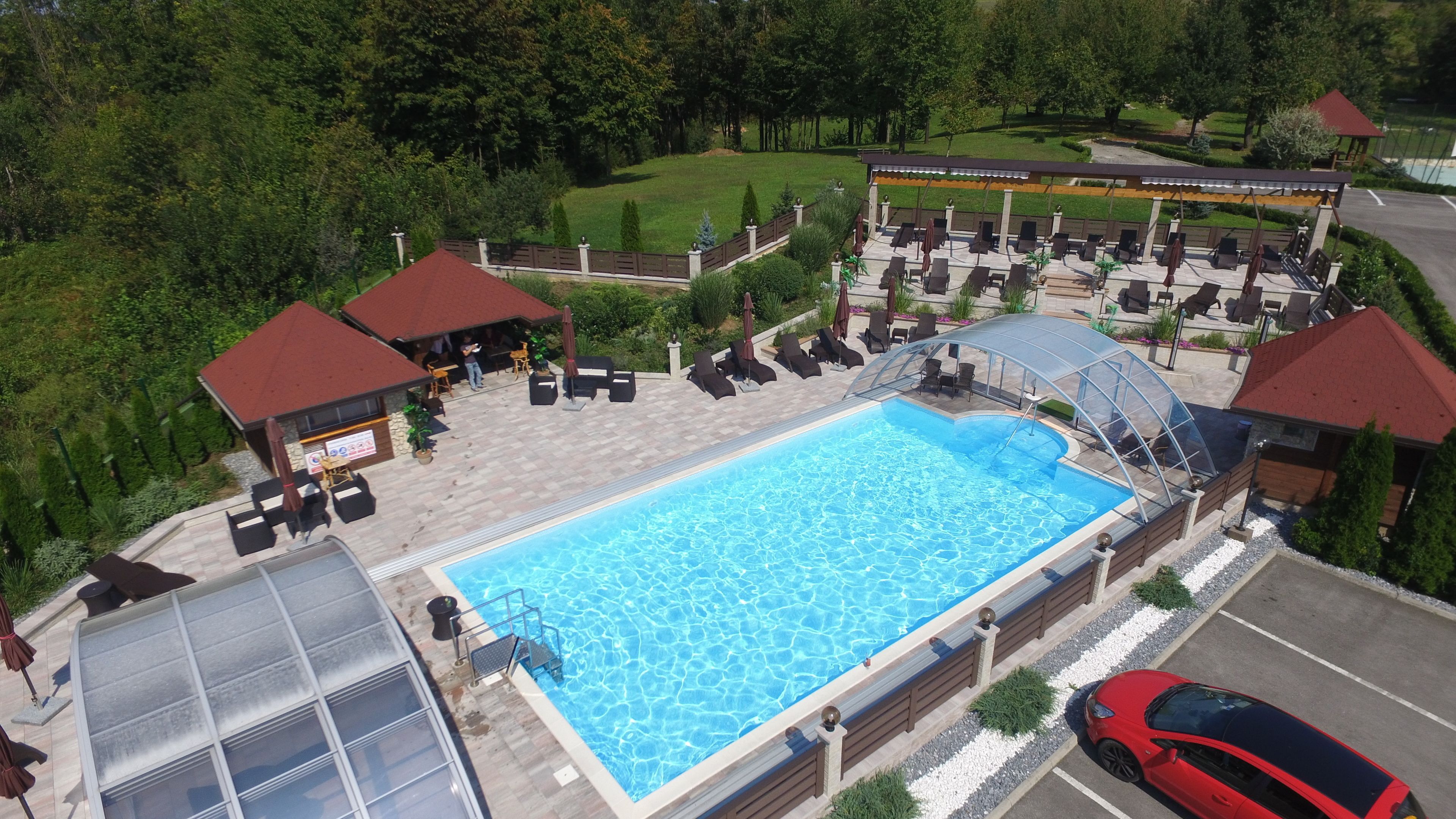 Ein Swimmingpool mit Liegestühlen und einer überdachten Sitzgruppe, umgeben von Grünflächen und einem Gebäude mit rotem Dach.