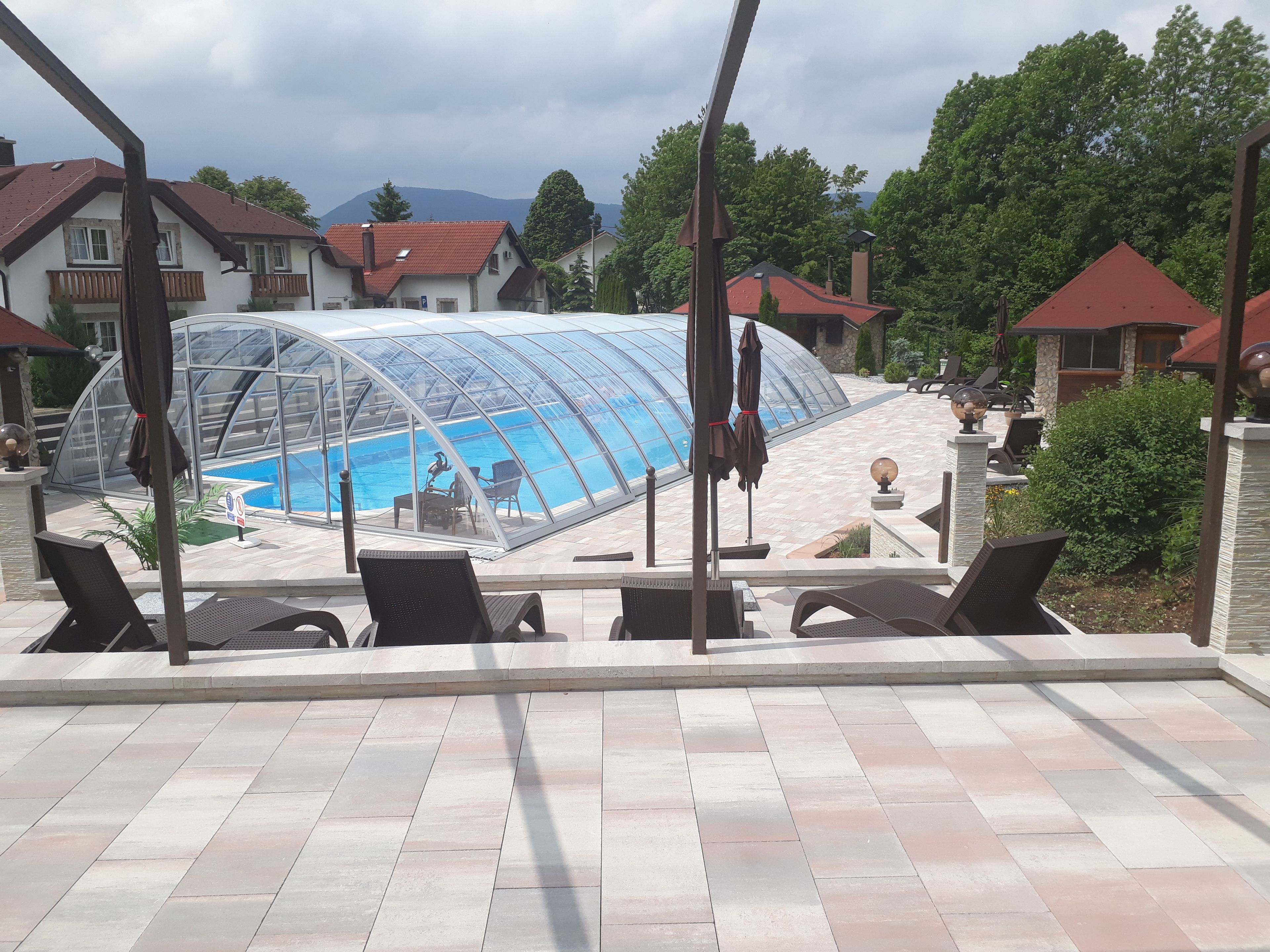 Ein Schwimmbad mit Glasveranda, umgeben von Liegestühlen und einer gefliesten Terrasse.