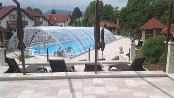 Ein Schwimmbad mit Glasveranda, umgeben von Liegestühlen und einer gefliesten Terrasse.