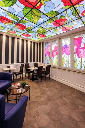 A room with hexagonal patterned flooring, a dining area with tables and chairs, and a ceiling with stained glass floral designs. - Barberini Suites (Rome)