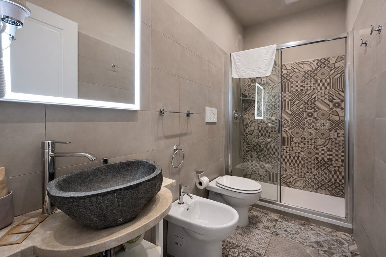Un baño con un lavabo de piedra, un bidé, un inodoro y una ducha con azulejos estampados.