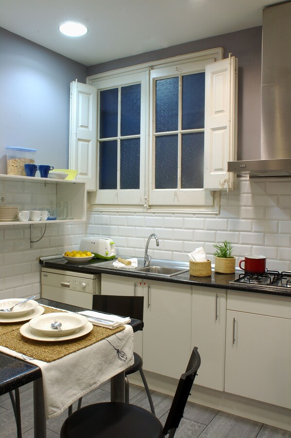 Una cocina con armarios blancos, encimera negra, ventana con vidrios azules y una taza roja sobre la encimera.