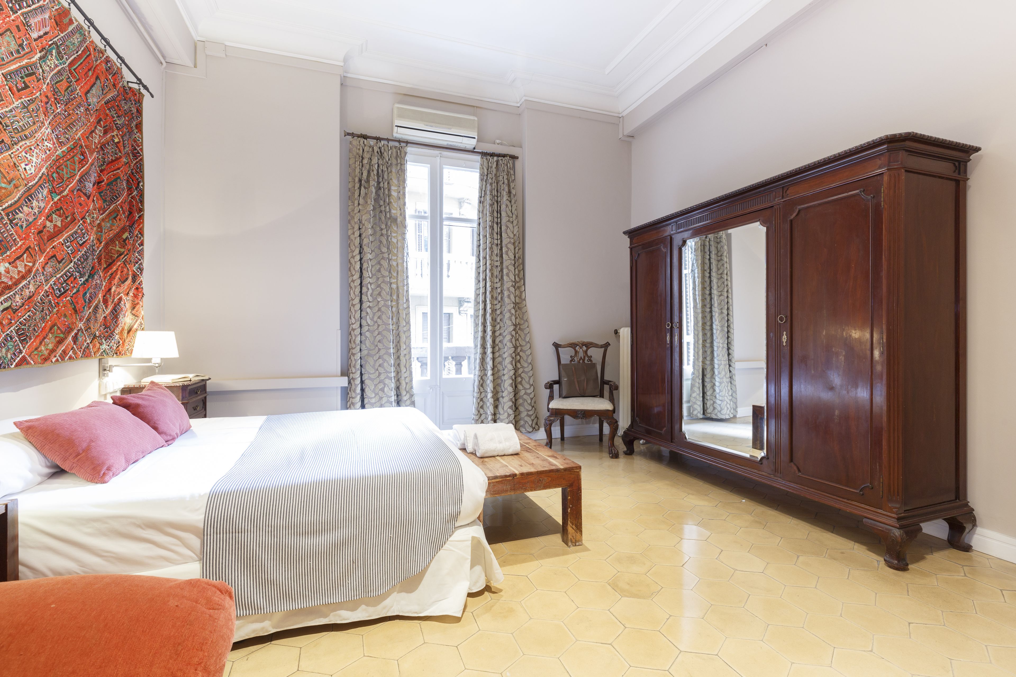 Een hotelkamer met een bed, een houten nachtkastje, een stoel, een grote spiegel en een kledingkast.