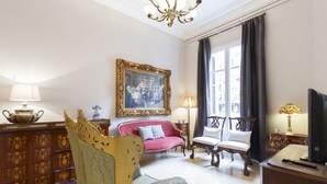 Une pièce avec un canapé rouge, un fauteuil bleu, un meuble en bois et un tableau accroché au mur.