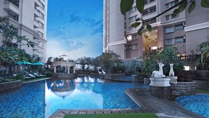 Pátio de hotel com piscina central, cercado por vegetação e elementos arquitetônicos.