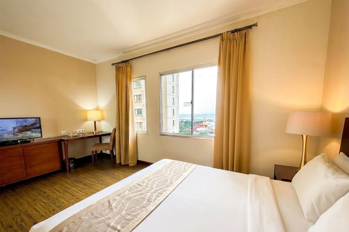 Une chambre d’hôtel avec un lit, un bureau, une télévision et une fenêtre avec des rideaux.